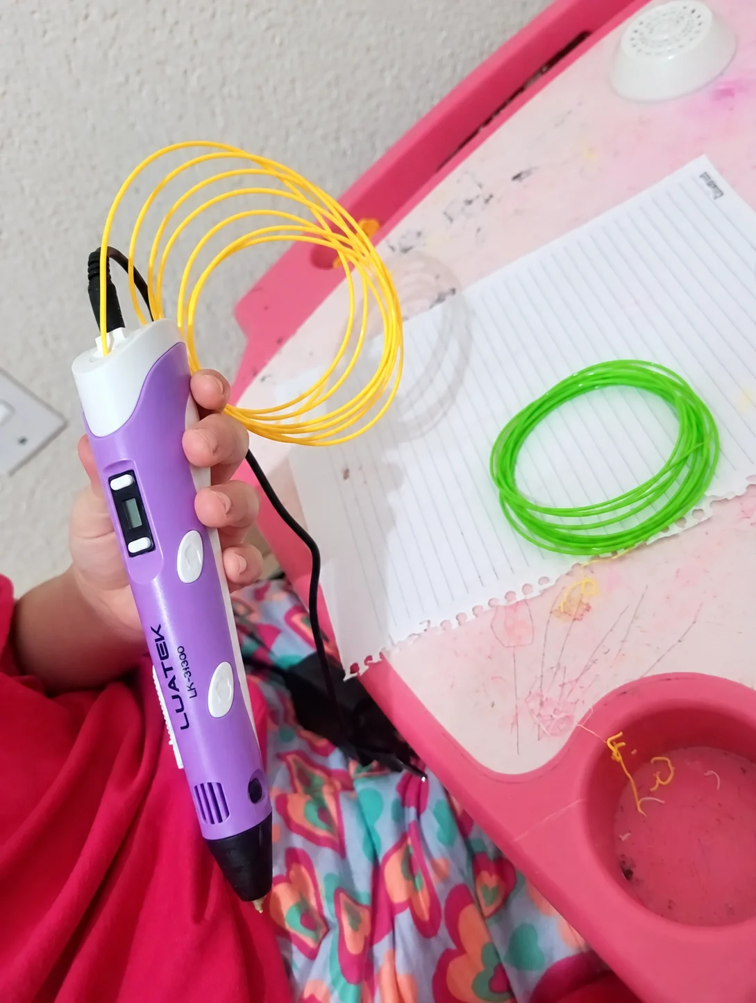 Imagem adaptada de uma mão segurando uma caneta 3D roxa ao lado de filamentos